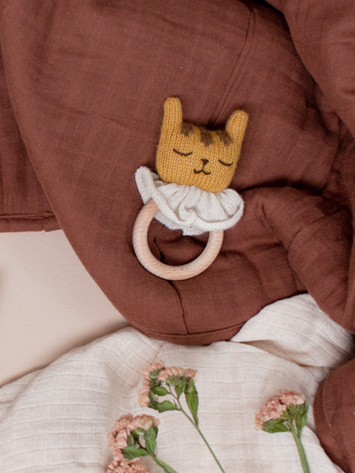 Knitted cat-shaped teething ring on a brown textured blanket with floral embroidery.