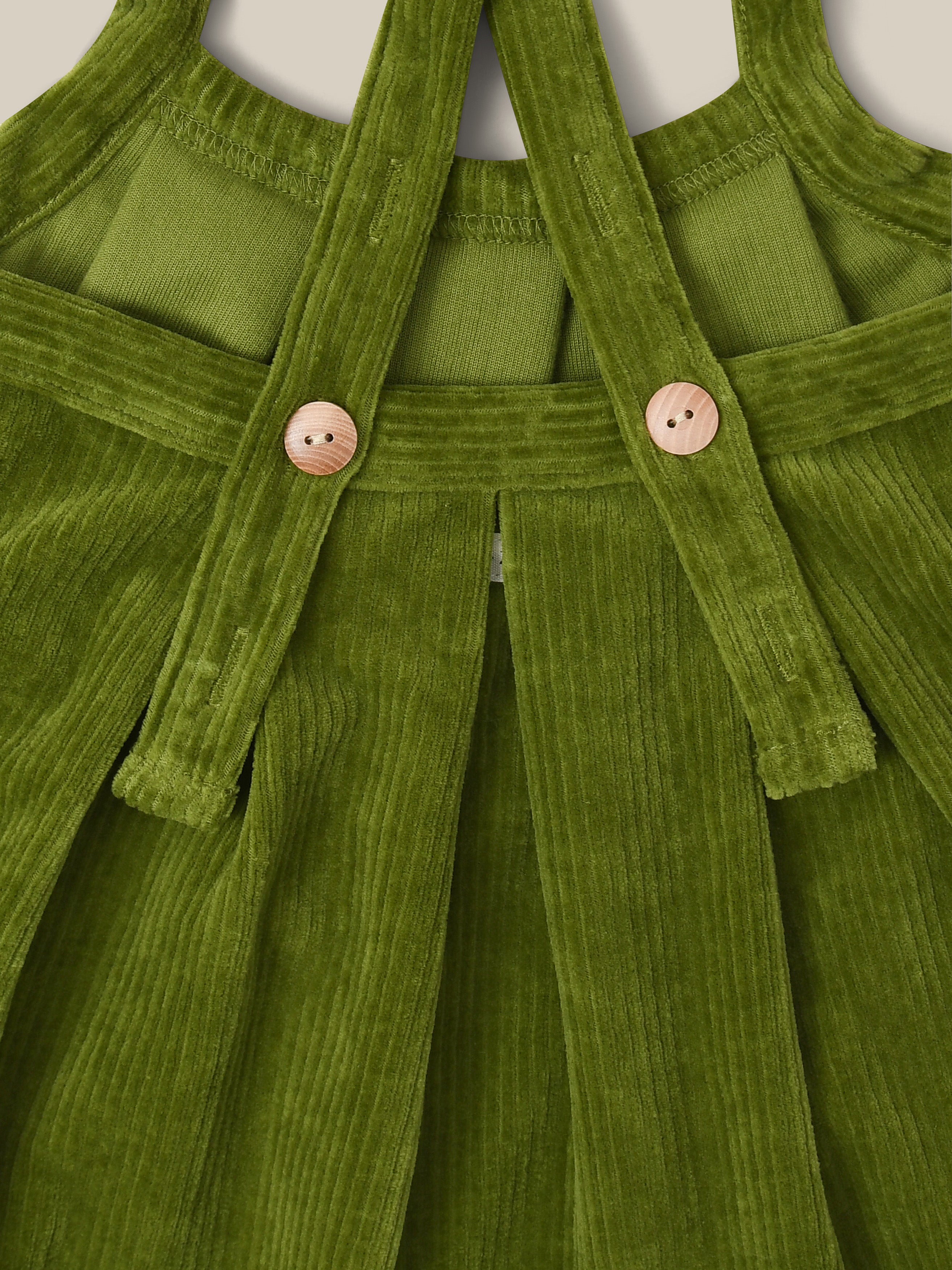 close up of cotton cord pinafore skirt in pea pod green with cross-back straps that are adjustable with buttons