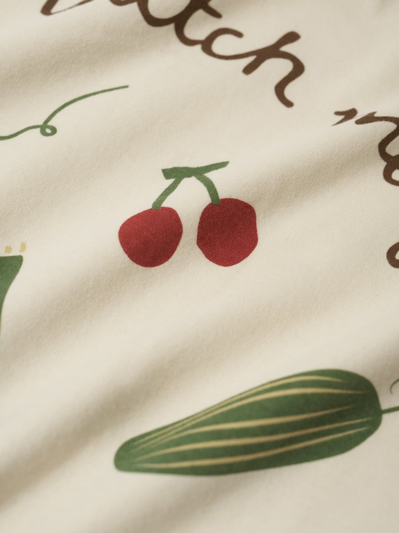 Close-up of fabric with cherry and cucumber illustrations on a beige background.