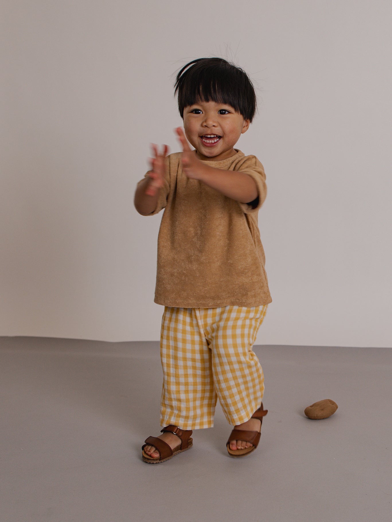 Child wearing a brown shirt and yellow checkered pants on a plain background