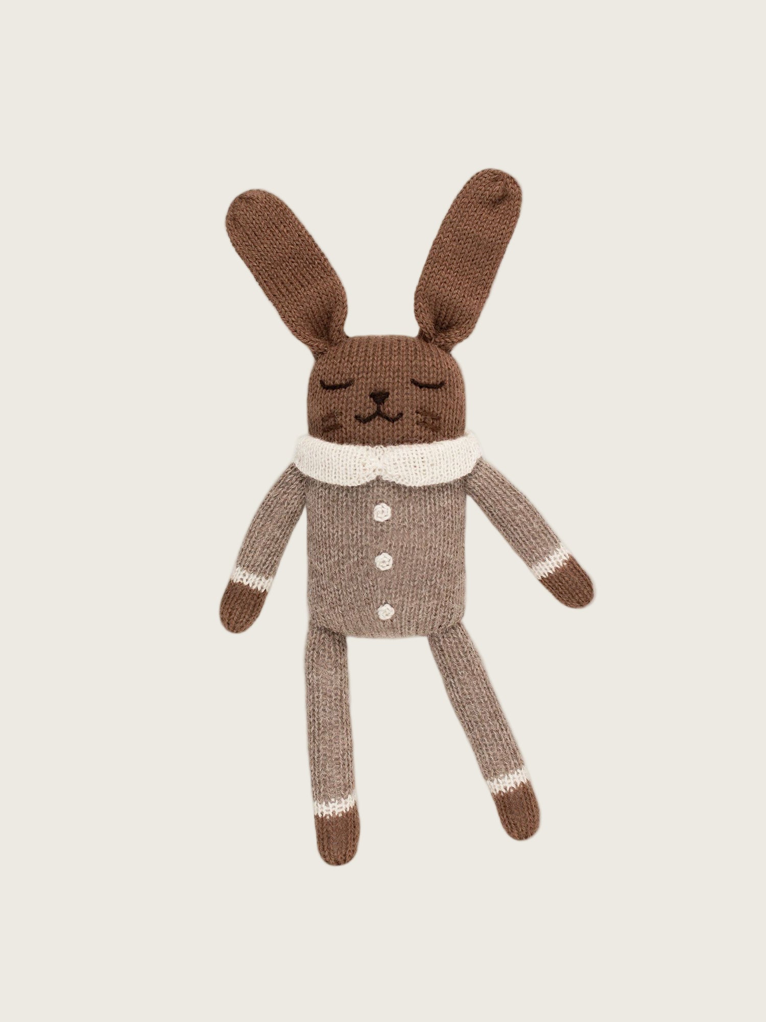 Hand knitted brown and beige baby bunny soft toy in an oat jumpsuit with a white collar and buttons.