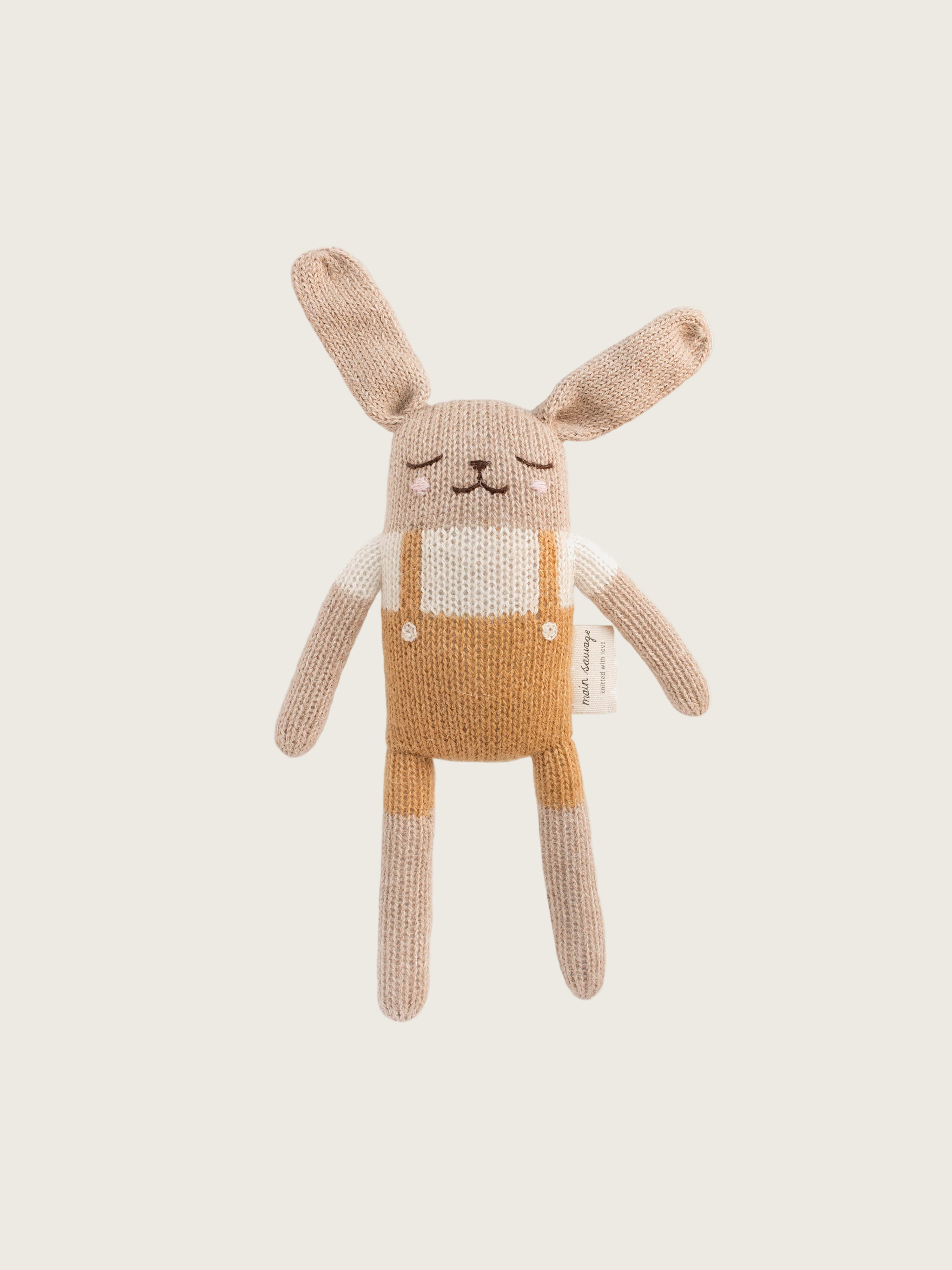 Hand knitted beige and mustard colored bunny soft toy with overalls.