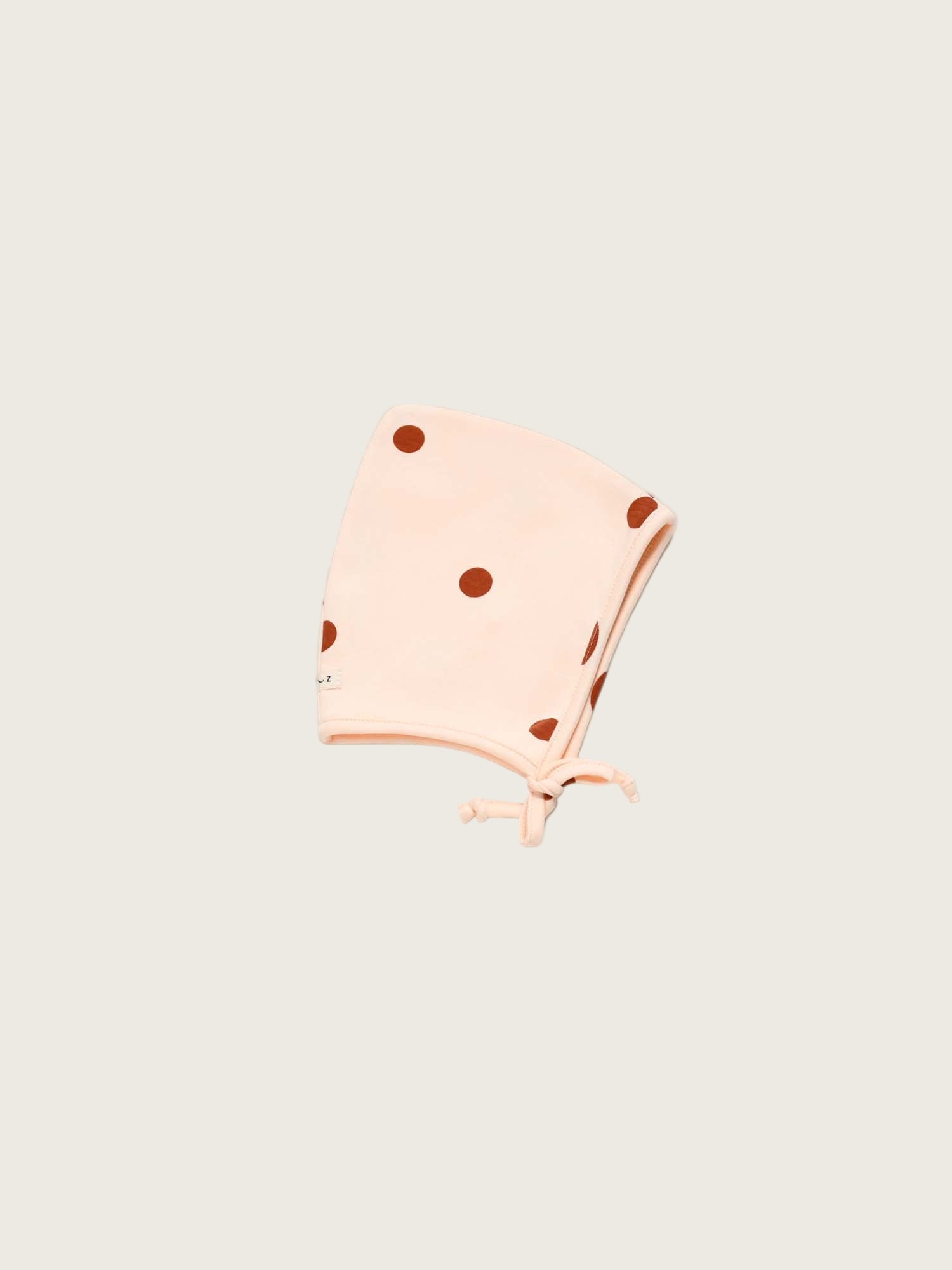 Pink polka dot baby bonnet on a light beige background