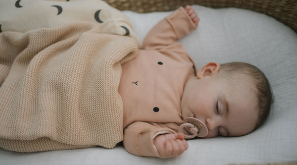 Baby in clay bunny playsuit sleeping in moses basket, swaddled in blanket