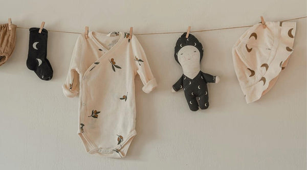 Biege baby bodysuit with olive print, doll, bucket hat and socks hanging on clothing line