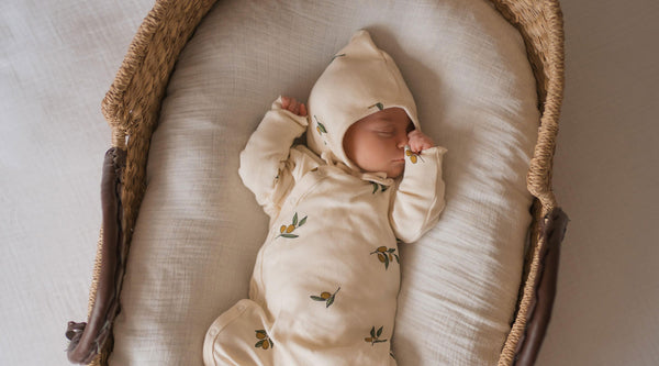 Baby in matching playsuit and bonnet with olive print sleeping in moses basket
