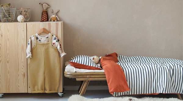 Child's bed with reversible stripes & red bedding, sweatshirt & dungaree hanging on cabinet & toys