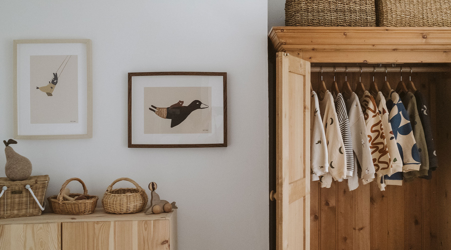 Baby clothes in wooden wardrobe in nursery room with baskets, toys, cabinet & paintings