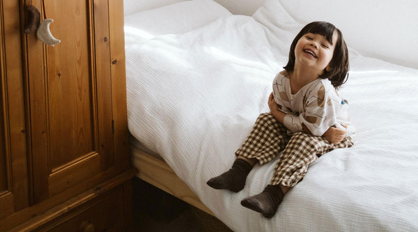Toddler wearing sweatshirt and brown gingham pants sitting on a bed