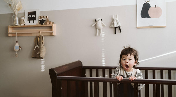 Toddler in striped sweatshirt and dungarees yawning and standing in cot