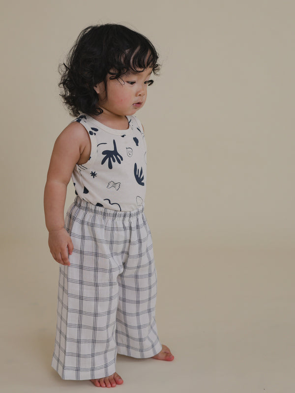 toddler wearing white summer vest with navy ocean print tucked into wide leg trousers looking down