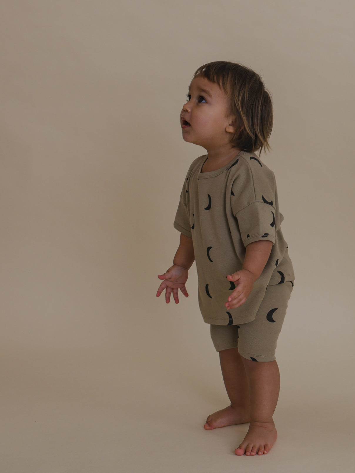 toddler in beige ribbed cotton biker shorts with black moons & matching top looking up
