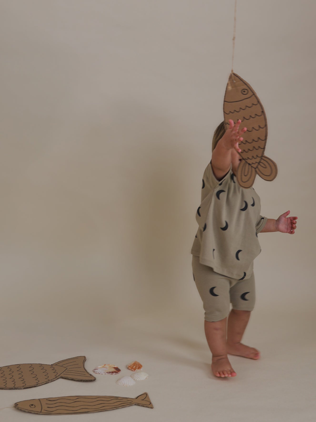 toddler in ribbed cotton dusky beige biker shorts with moon print reaching for cardboard fish