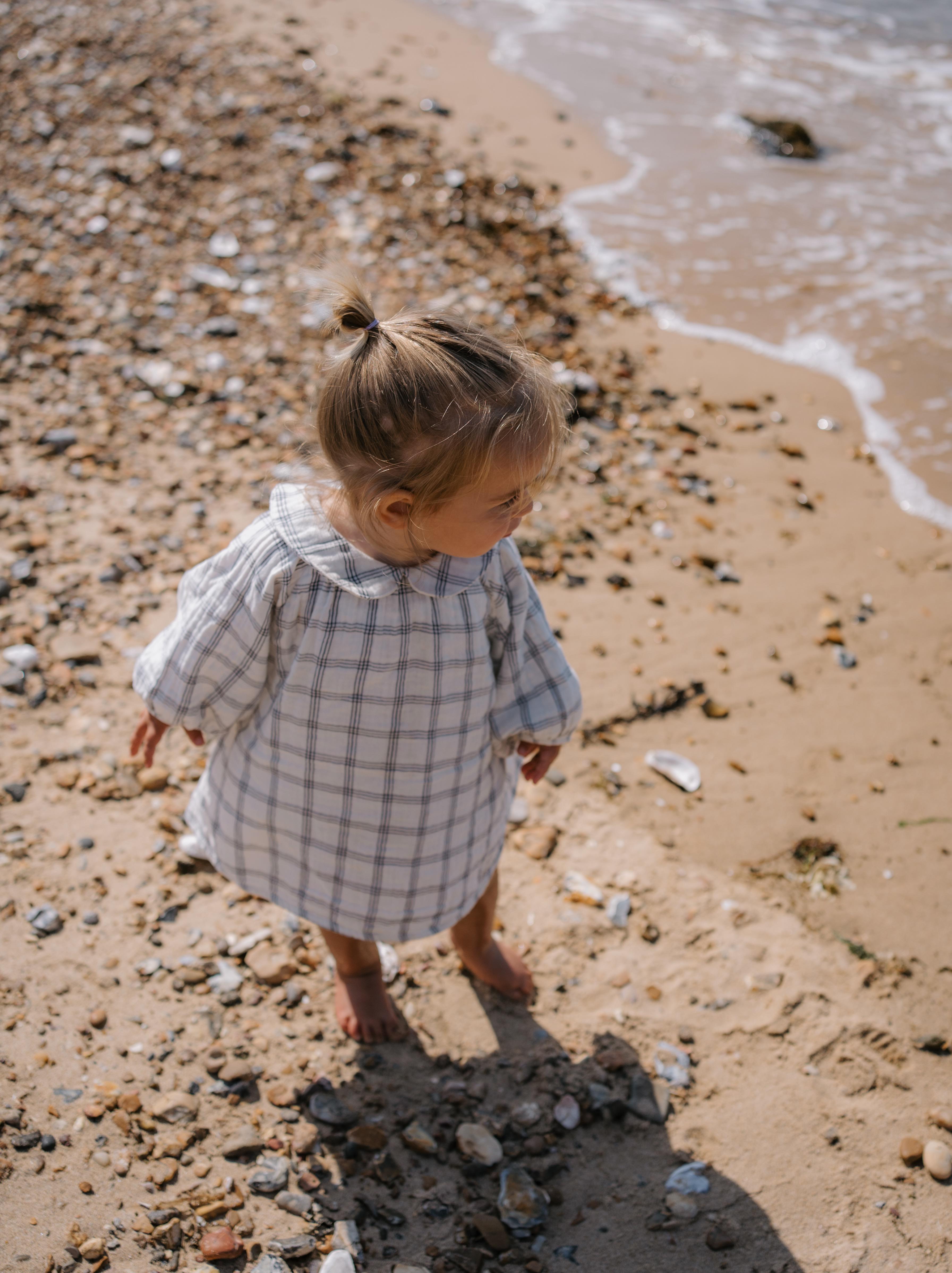 baby girl in navy window check long sleeved muslin button-down white dress, with peter pan collar & gathered cuffs