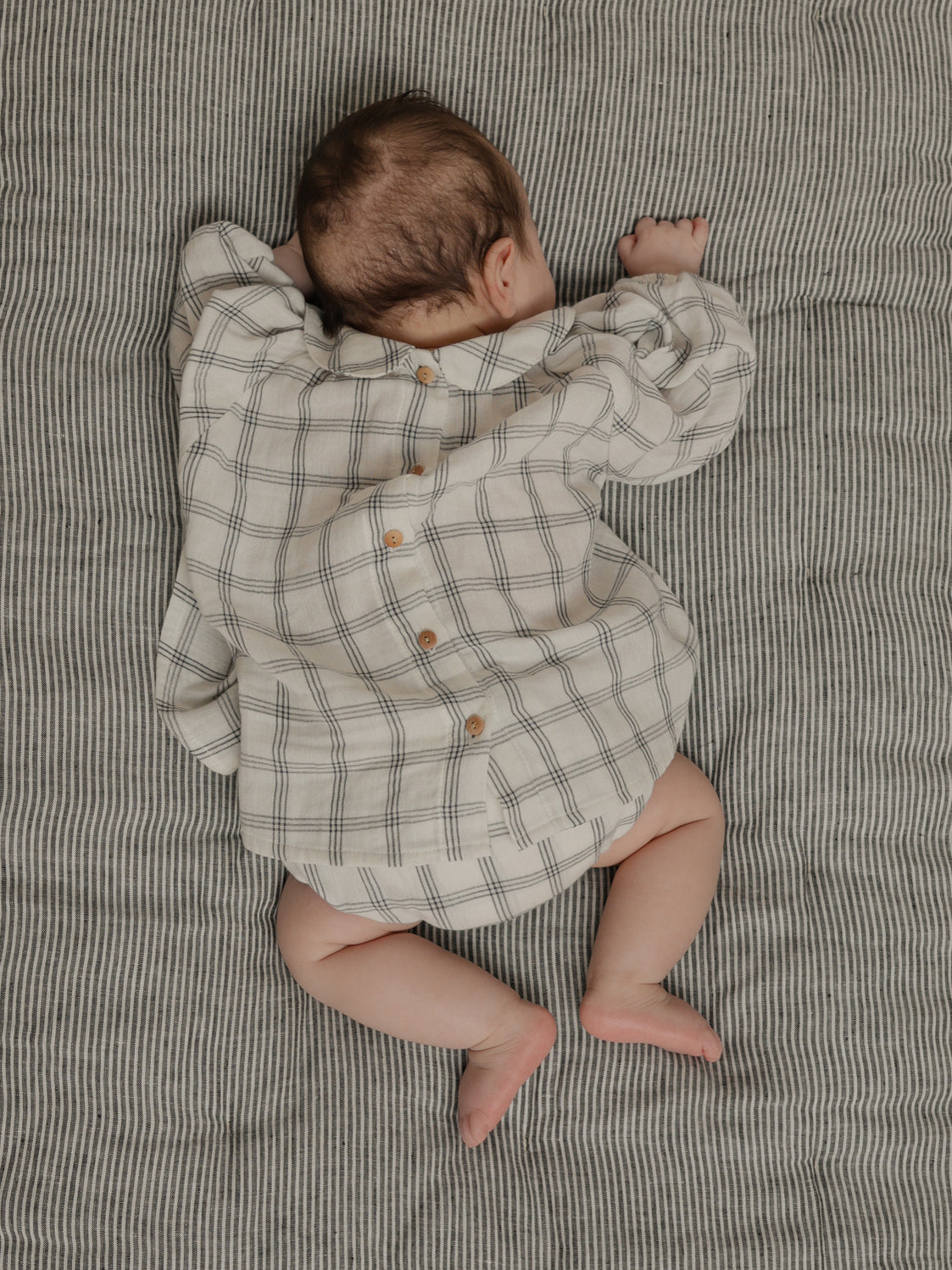 baby wearing long sleeved collar button down dress with navy window check print sleeping face down