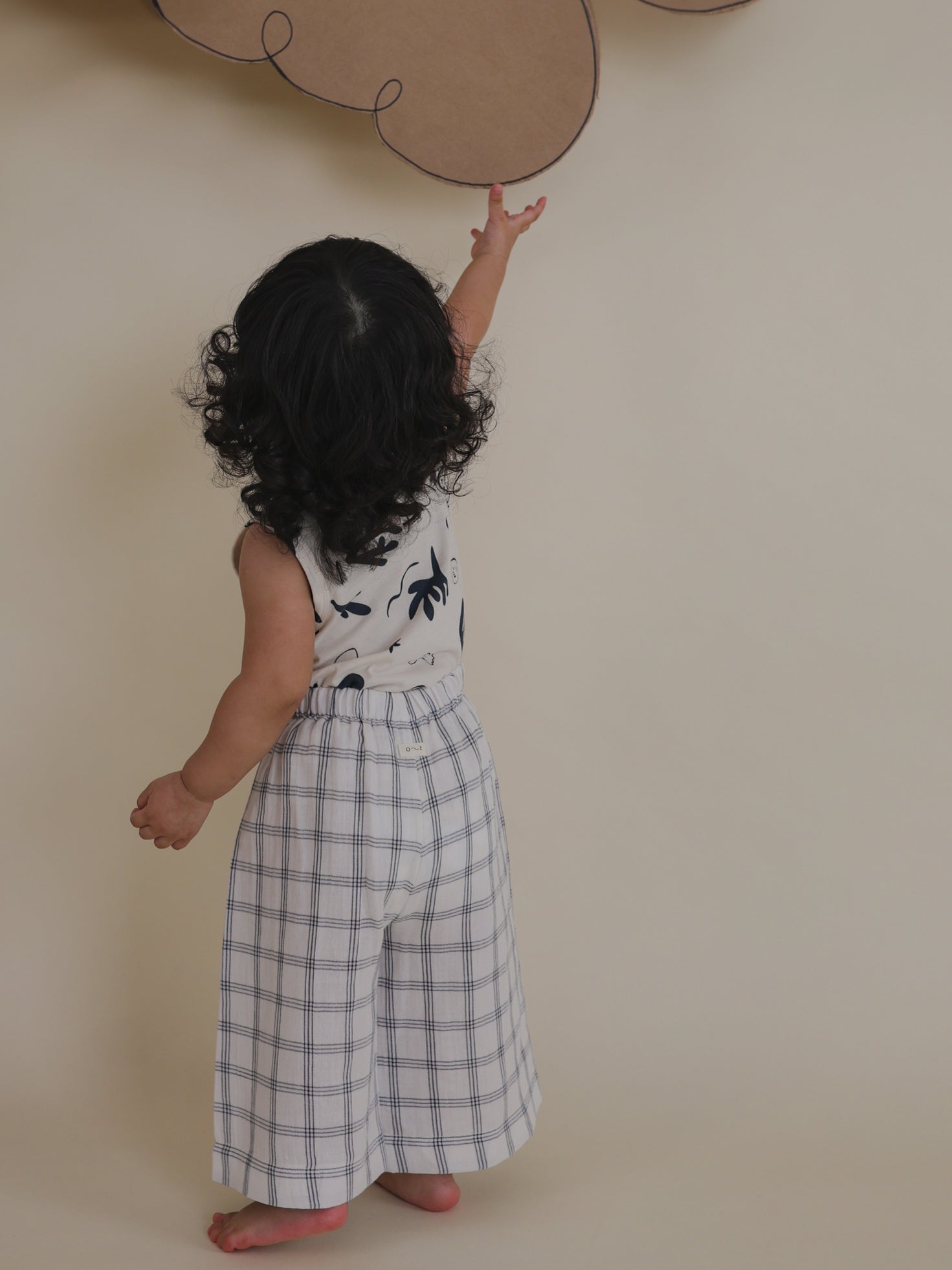 toddler in navy window check print wide leg trousers tip toe reaching for item