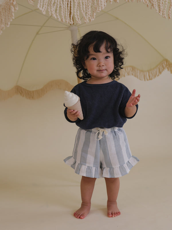 toddler in sardine blue striped drawstring frill shorts with navy top holding toy ice cream