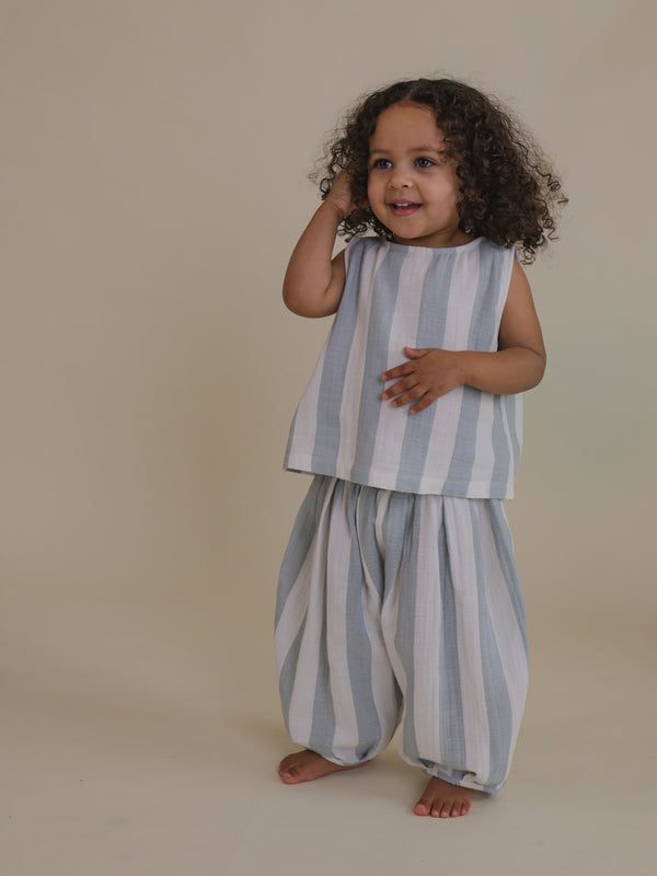 toddler wearing matching blue striped sleeveless muslin ribbon-tie top & barrel trousers hand on head