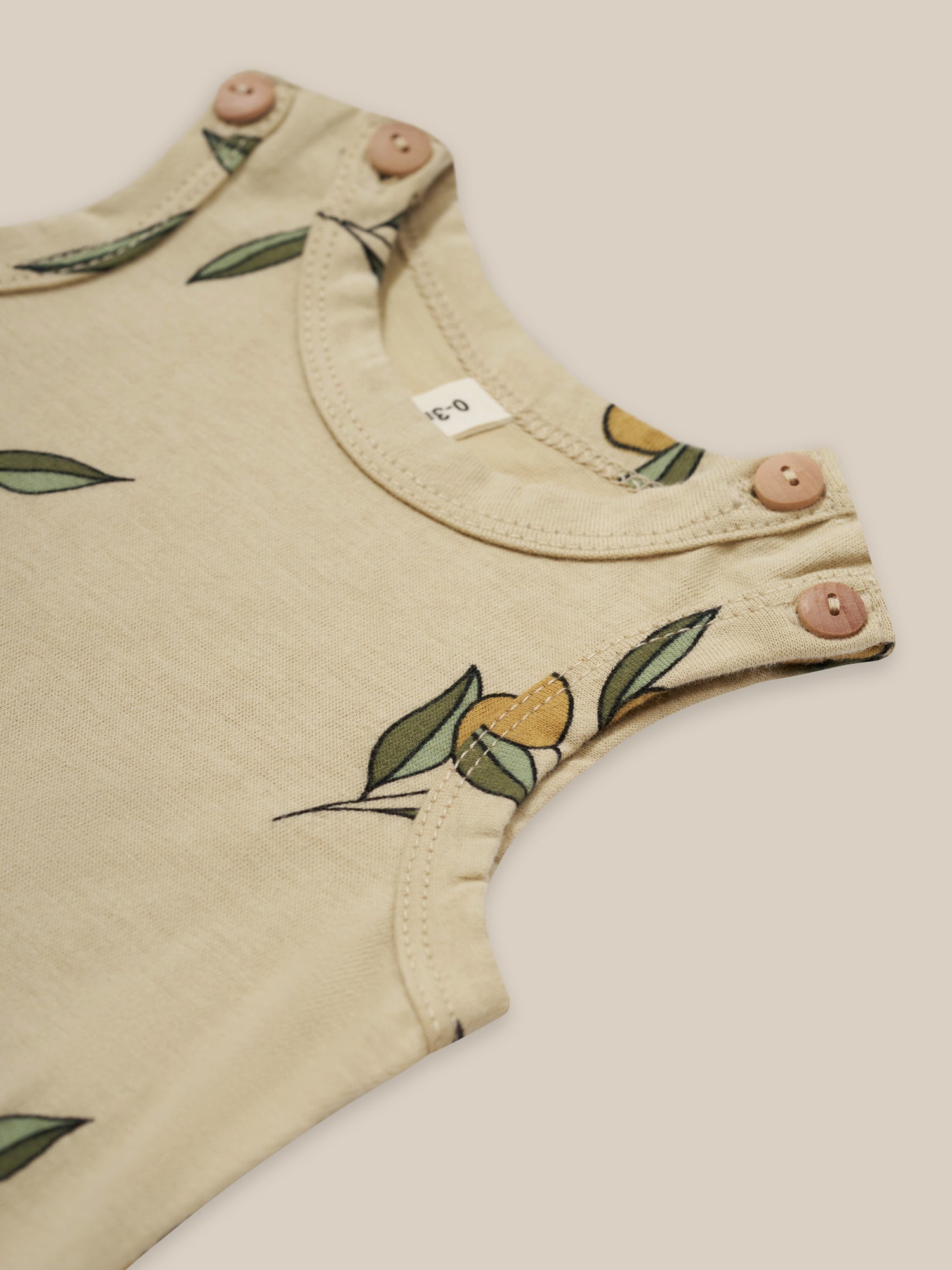 close up of baby organic cotton sleeveless cream bodysuit with olive print & shoulder buttons
