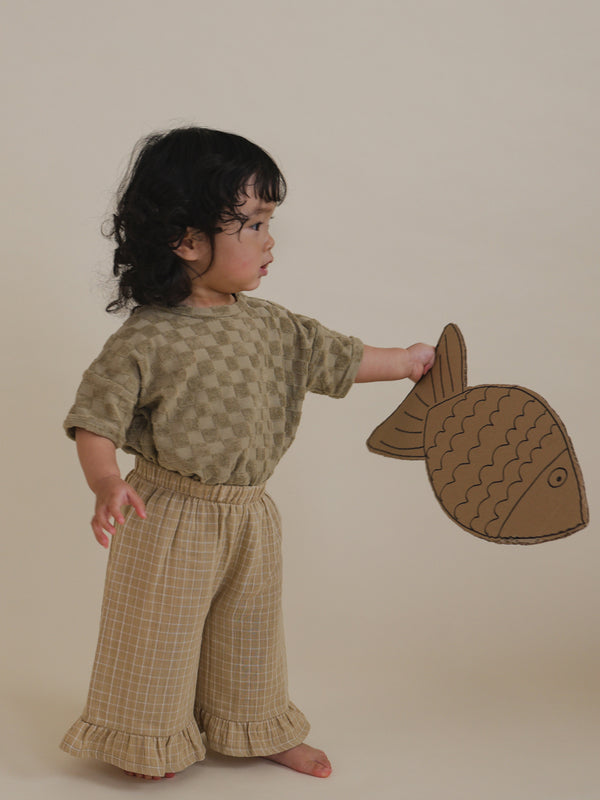 toddler in dusky beige checkerboard drop shoulder t-shirt tucked in pants, holding cardboard fish