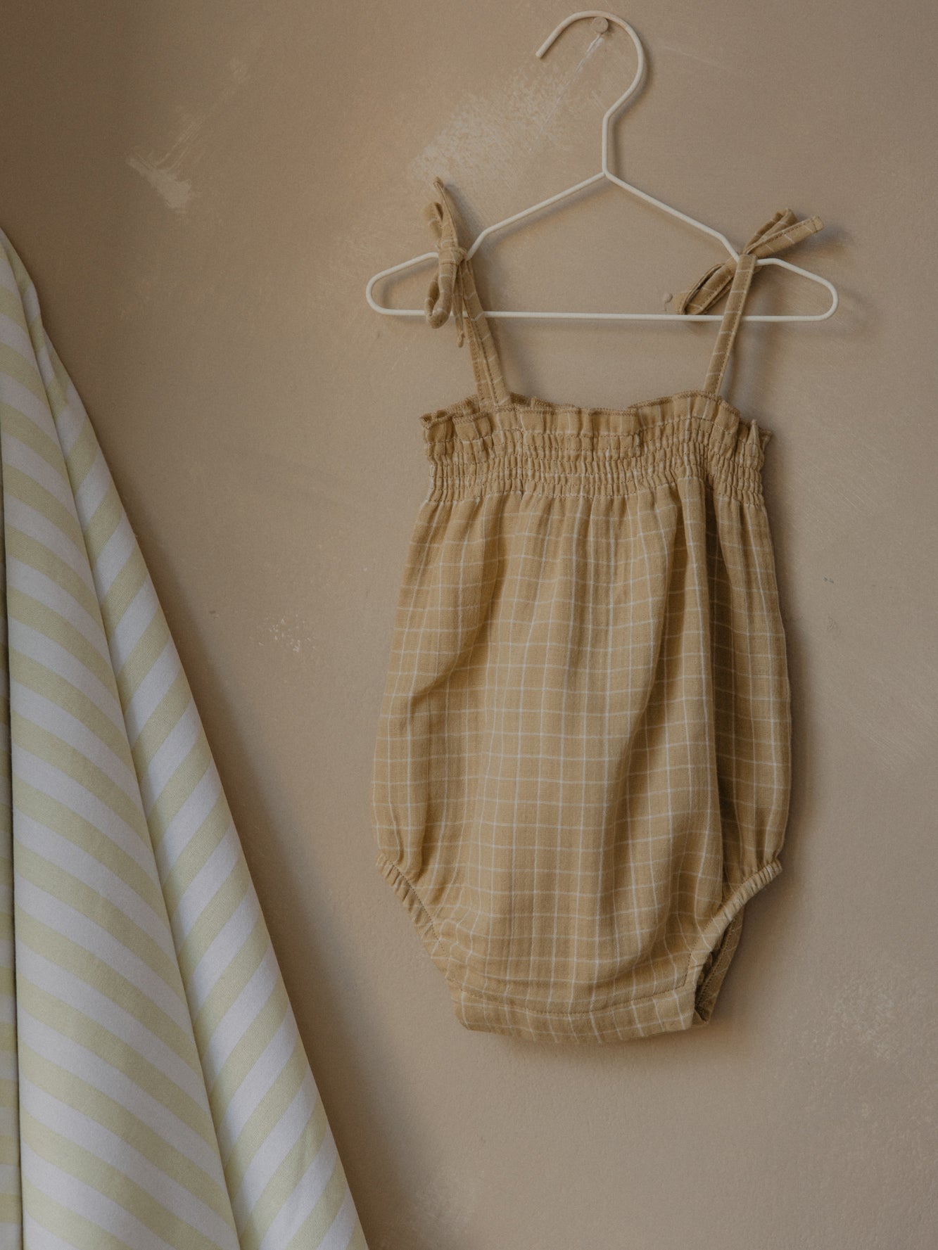 baby gold grid check muslin bodysuit with smocked neckline, spaghetti shoulder tie straps on hanger