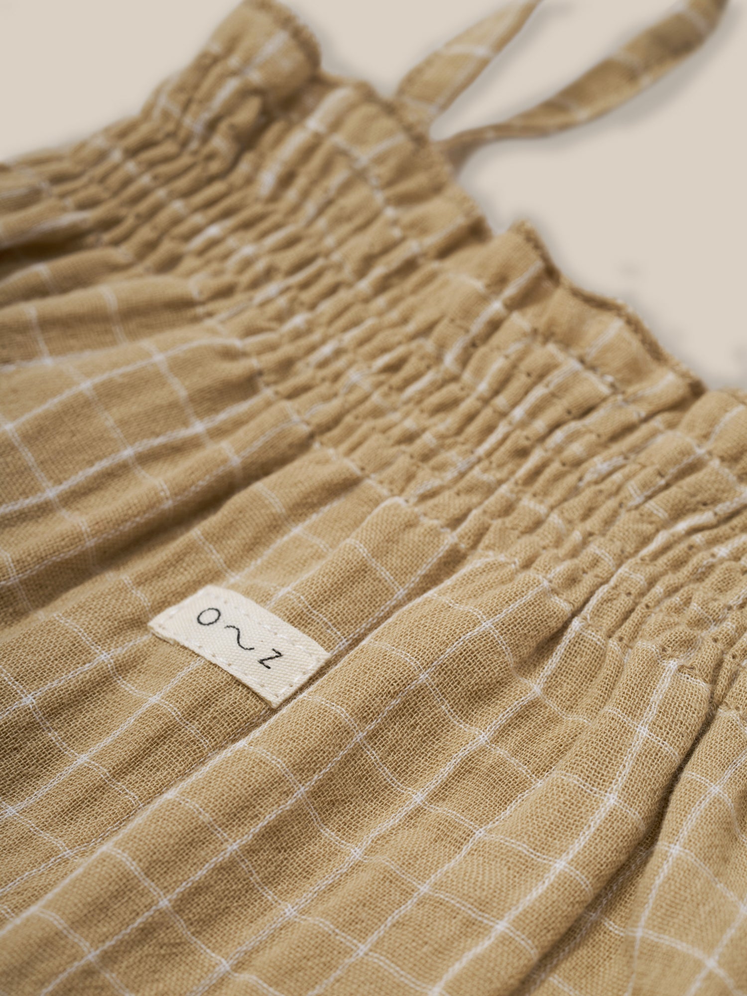 close up of baby gold grid check organic muslin bodysuit with smocked neckline & spaghetti straps