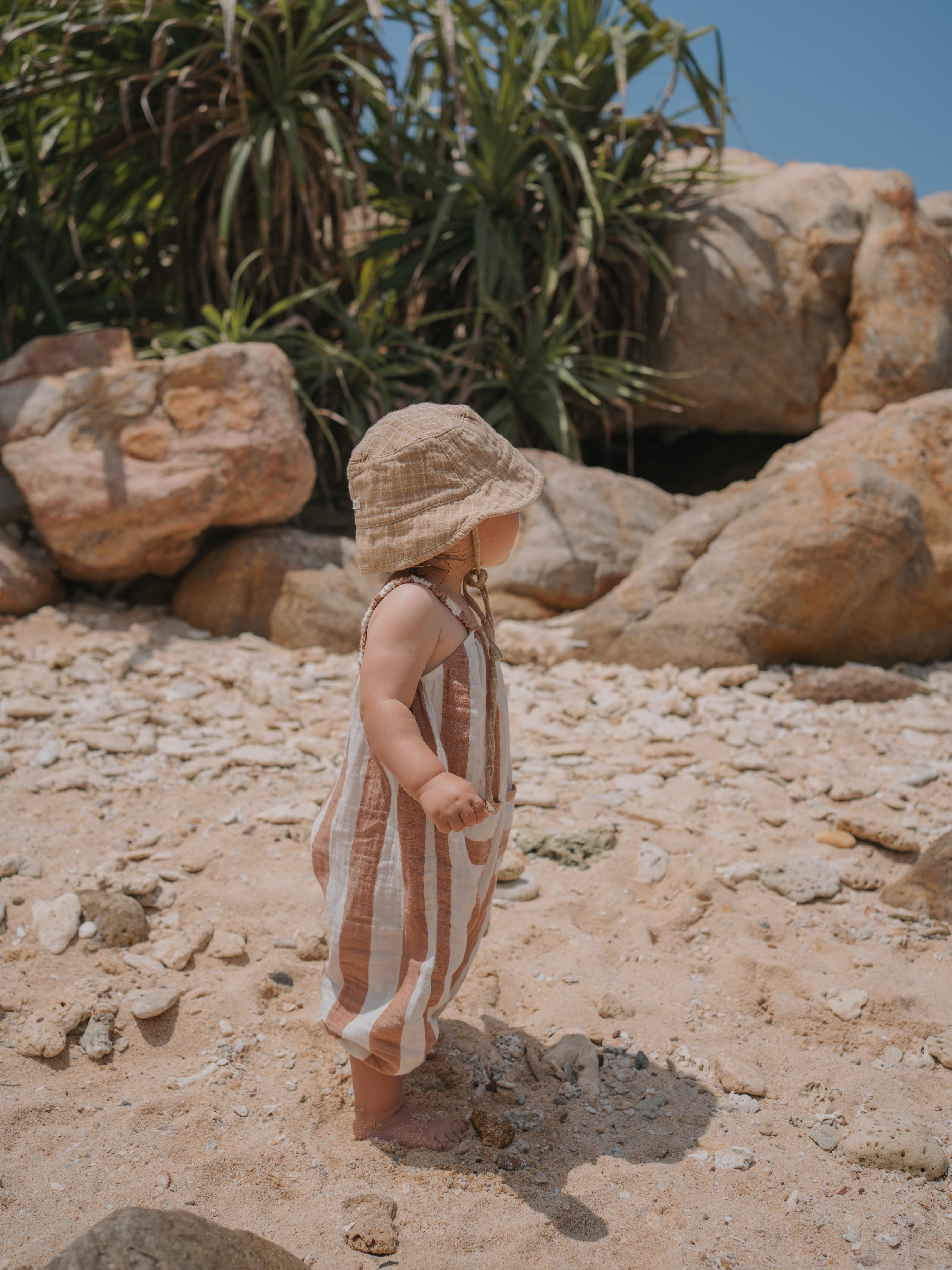 baby in sienna red striped muslin jumpsuit with gathered straps on the beach