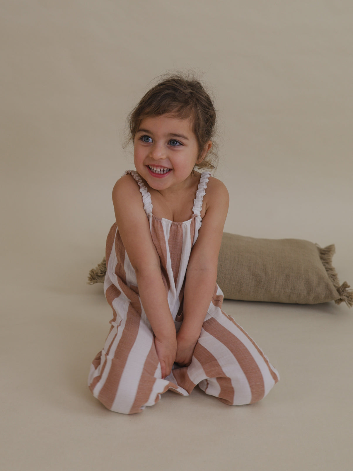toddler smiling in soft muslin jumpsuit with sienna red stripes & gathered straps