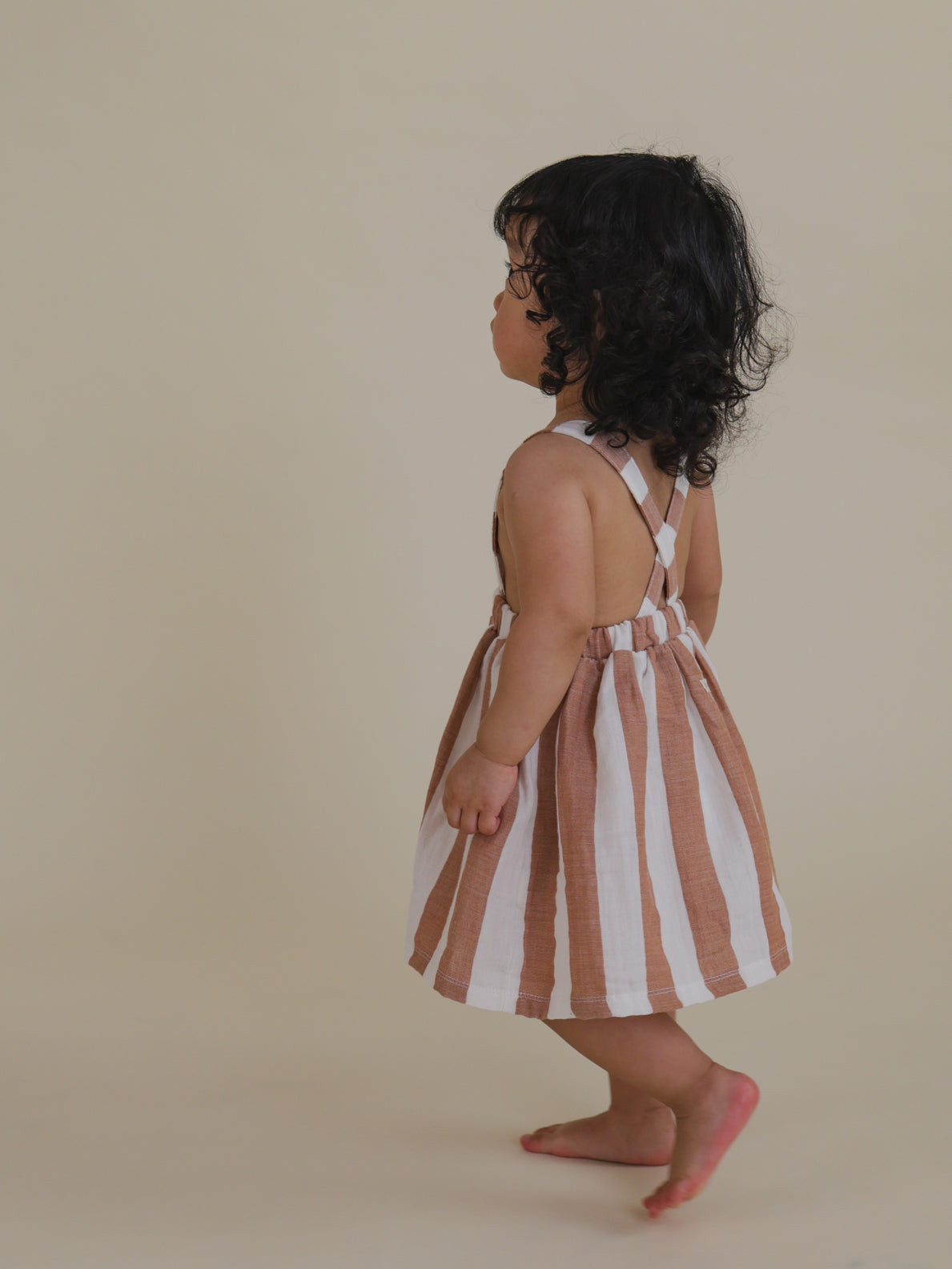 toddler strolling in a playful red & white striped apron skirt with crisscross straps
