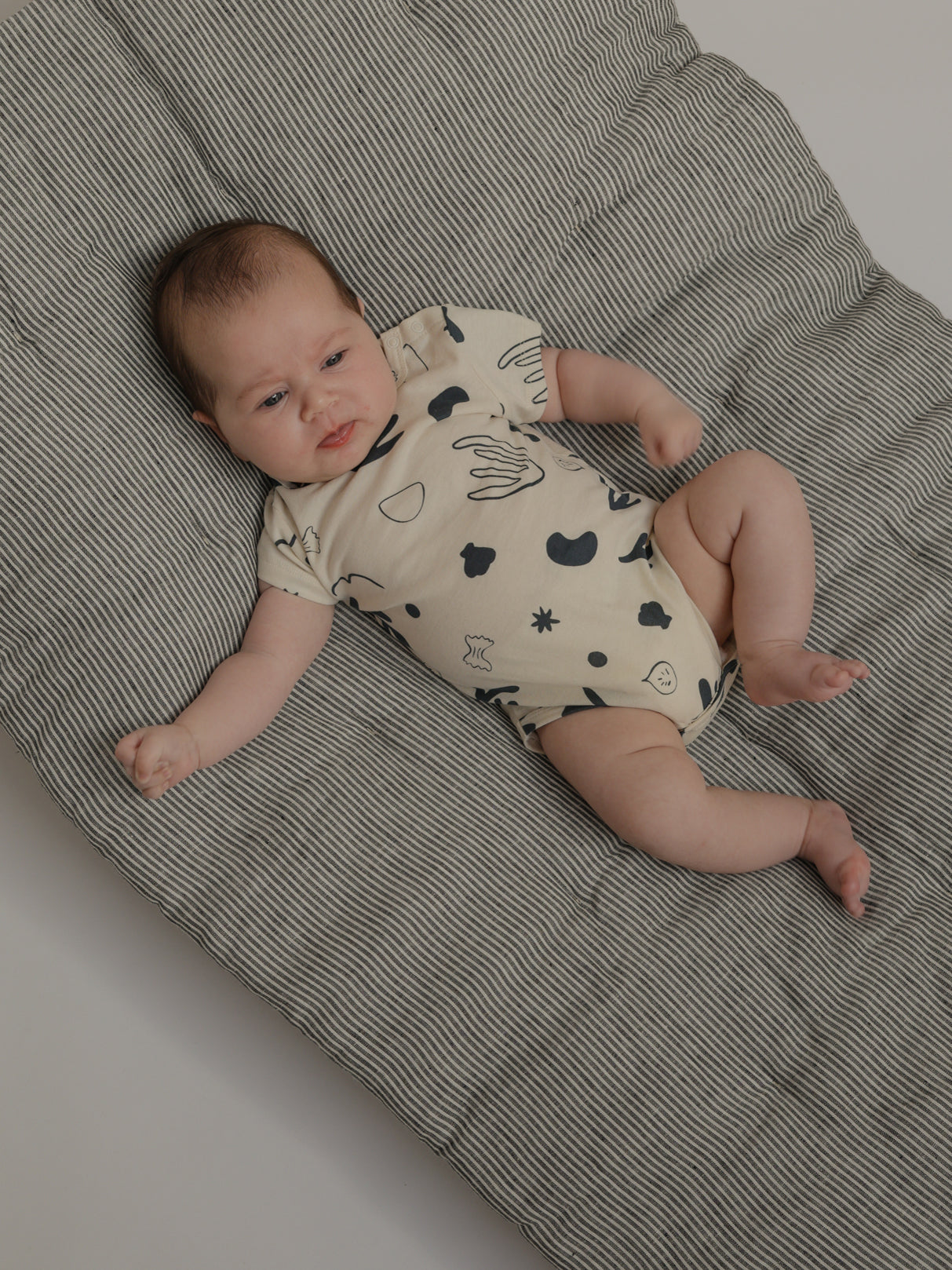 baby in white short sleeved bodysuit with navy capri ocean print lying on mattress