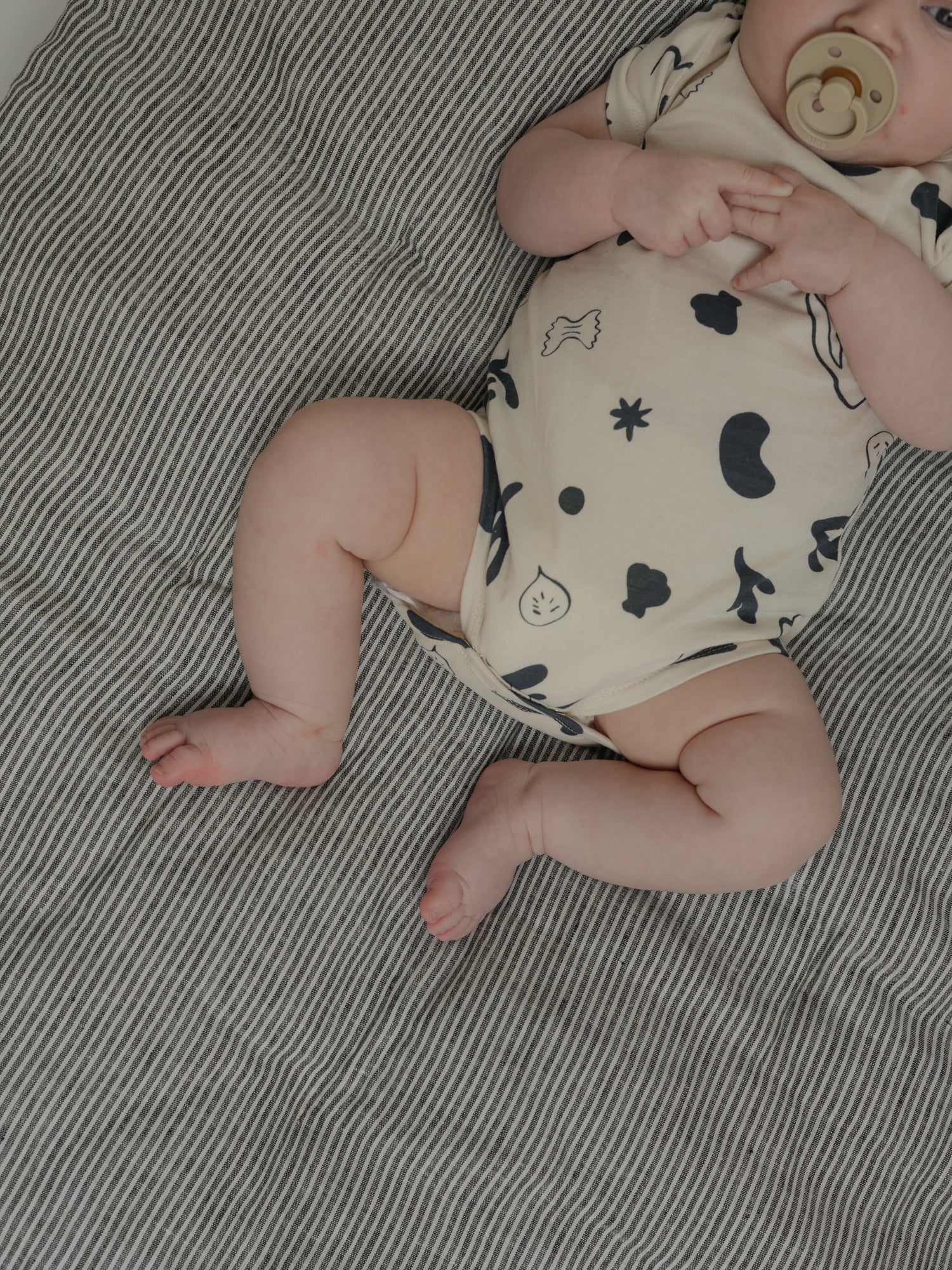 baby in short sleeved undyed cotton ocean print bodysuit with pacifier, hands held together