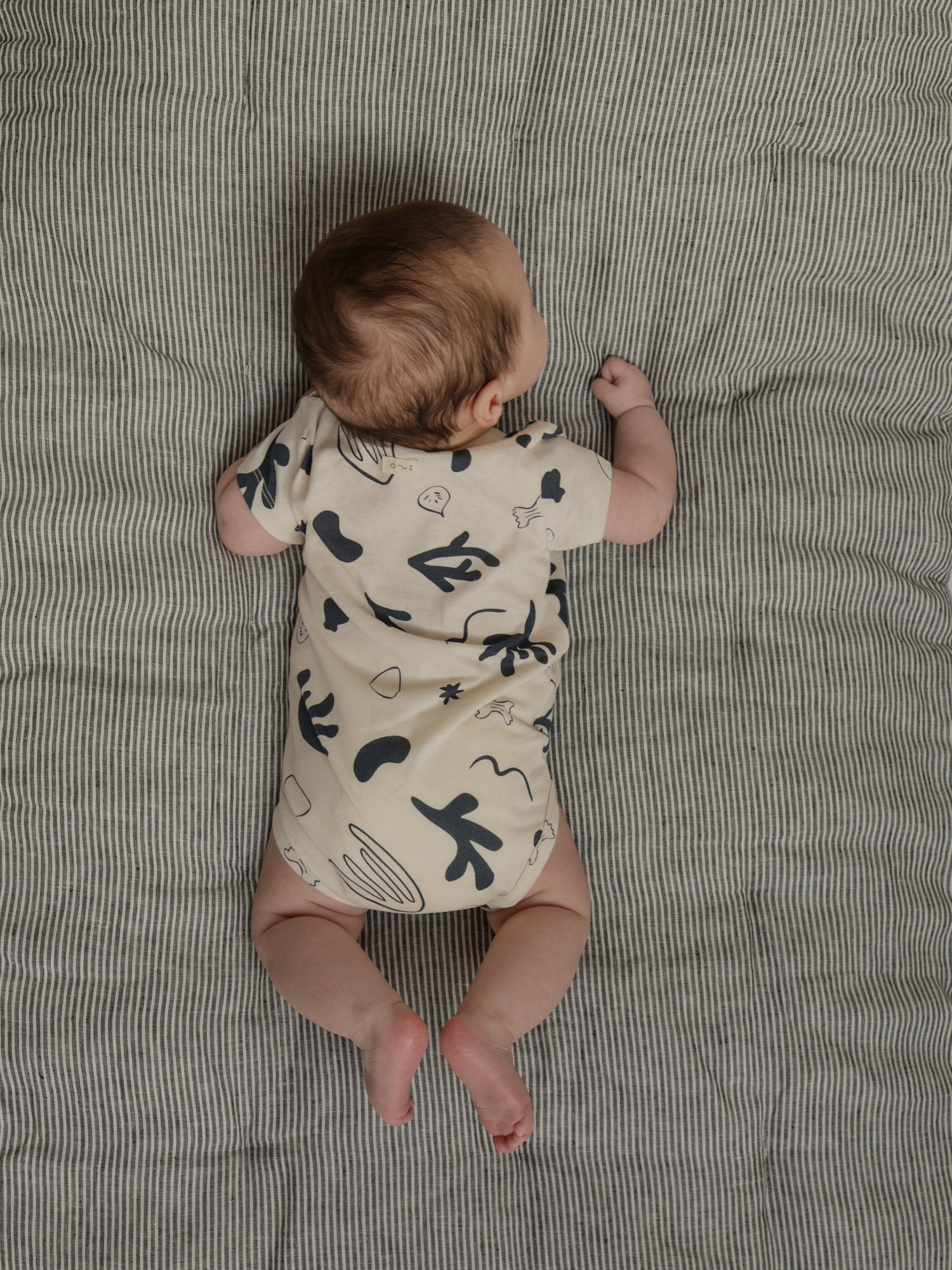 baby wearing white short sleeved undyed cotton bodysuit with ocean print tummy time