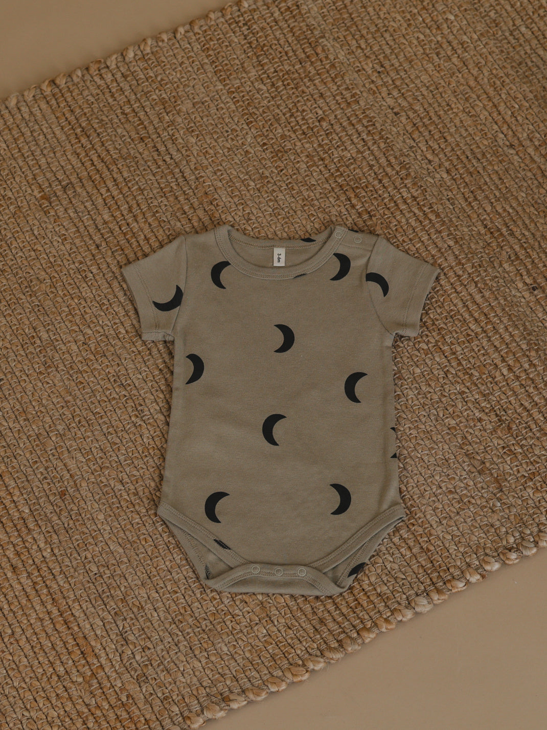 baby dusky beige organic ribbed cotton short sleeved bodysuit with black moon print on rustic woven mat
