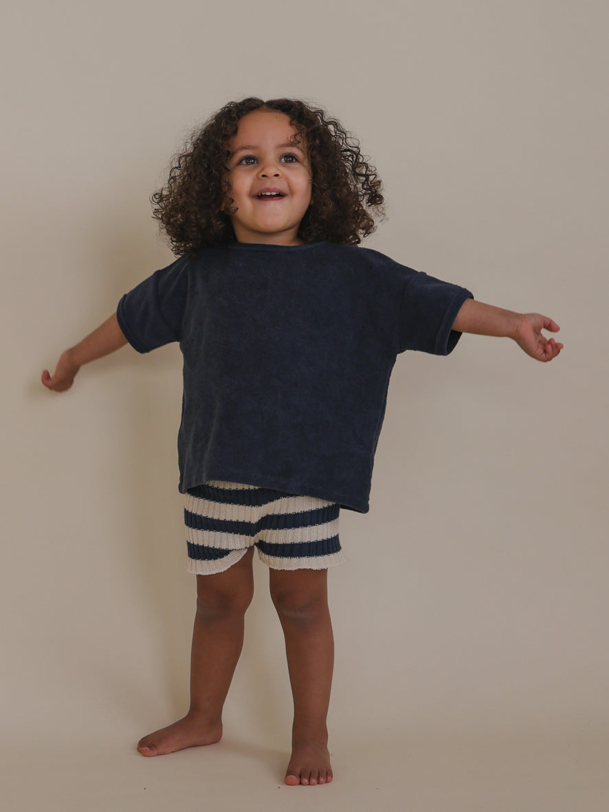 happy toddler in navy sailor striped knitted shorts & t-shirt standing with arms open