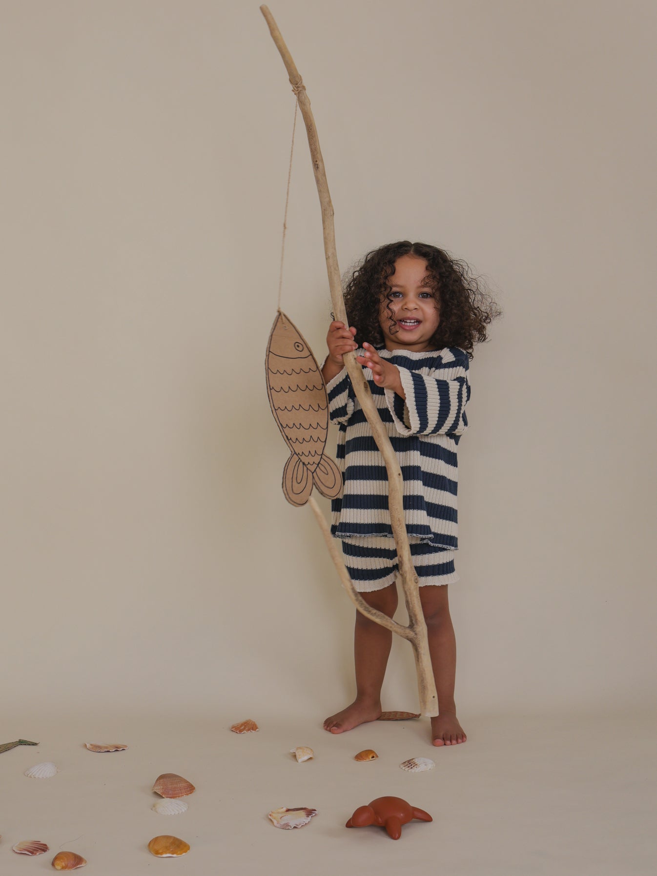 toddler in matching rib knitted navy striped shorts & sweater holding branch with cardboard fish