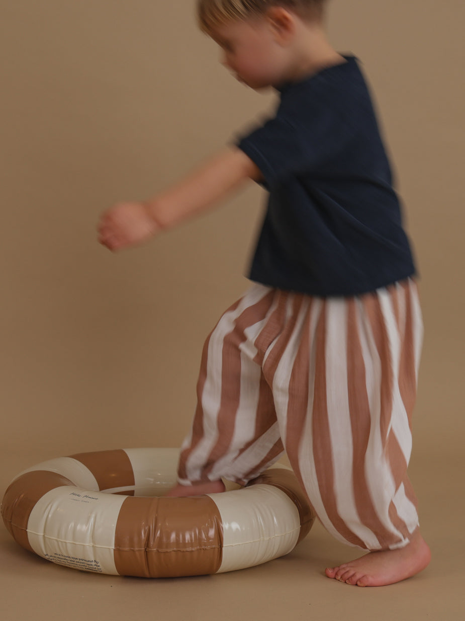 toddler in soft muslin barrel resort trousers with fun sienna red stripes hopping into pool ring