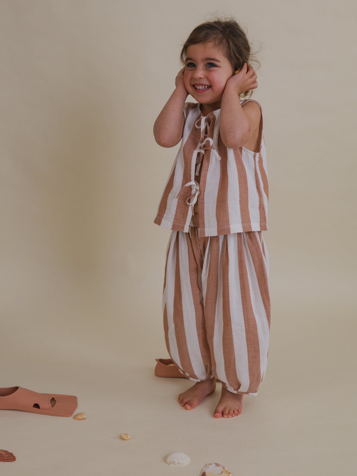 toddler in soft muslin red striped barrel resort pants & front-tie top covering ears