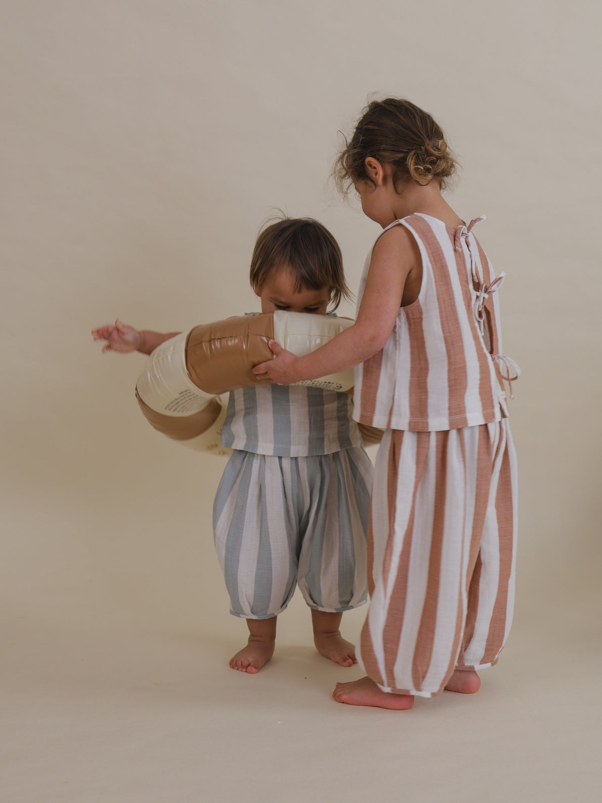 child in sienna red striped resort muslin pants & ribbon-tie back top putting pool ring on toddler