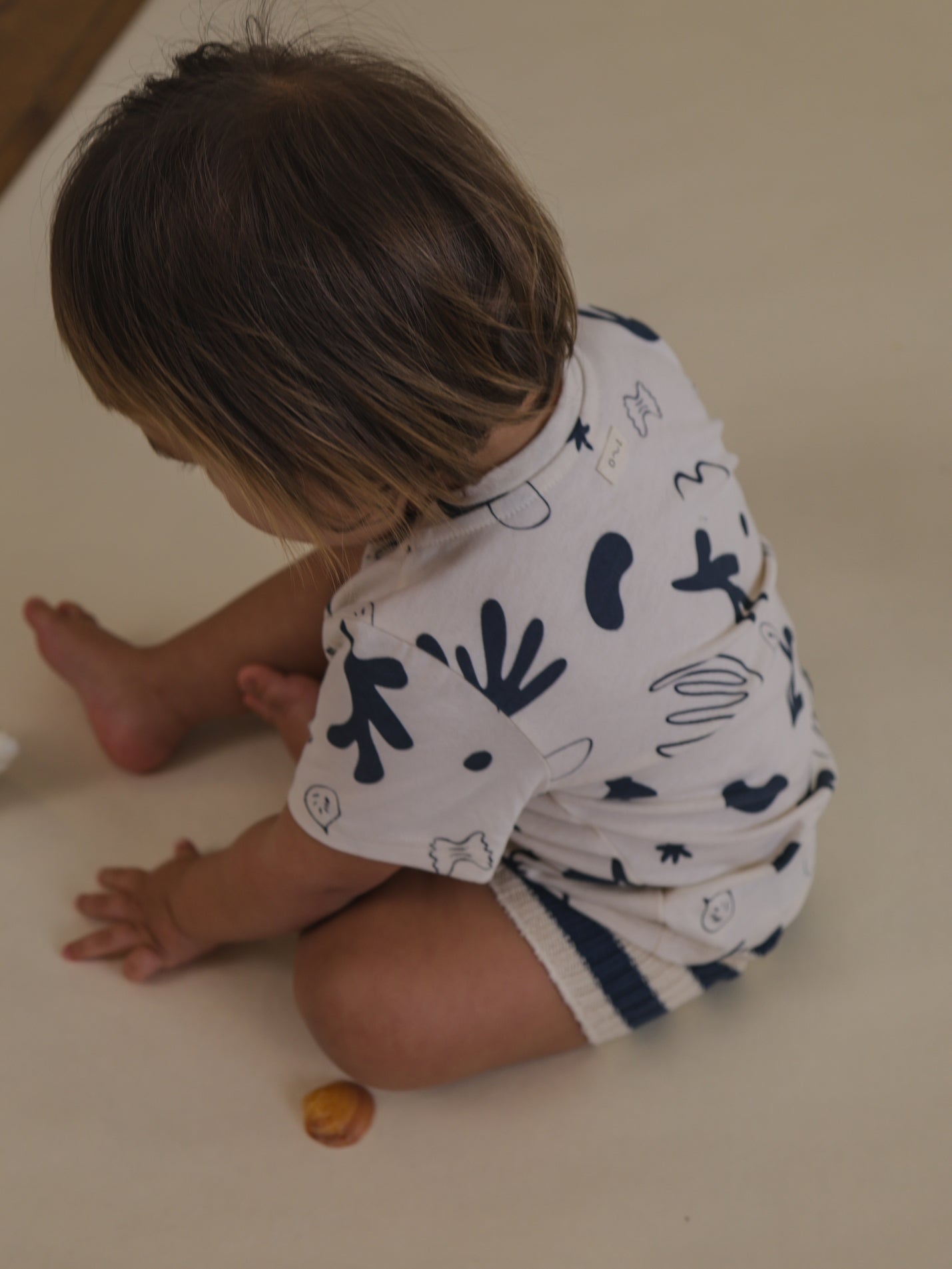 toddler in white short sleeved undyed cotton crew neck t-shirt with navy ocean print sitting on floor playing