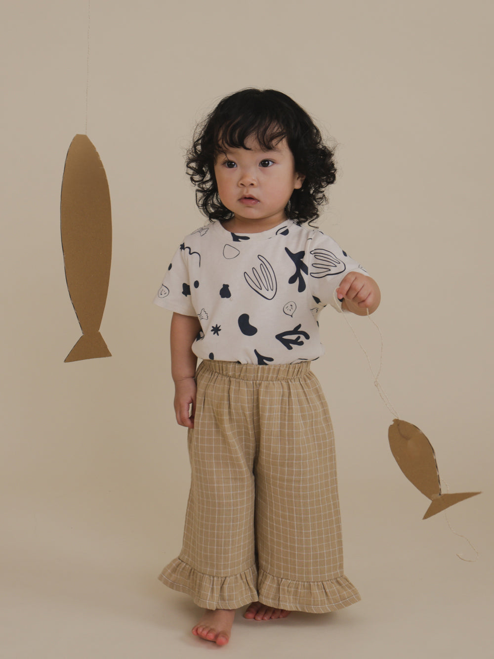 toddler in capri crew neck t-shirt with ocean print tucked in trousers, pretend play with cardboard fish