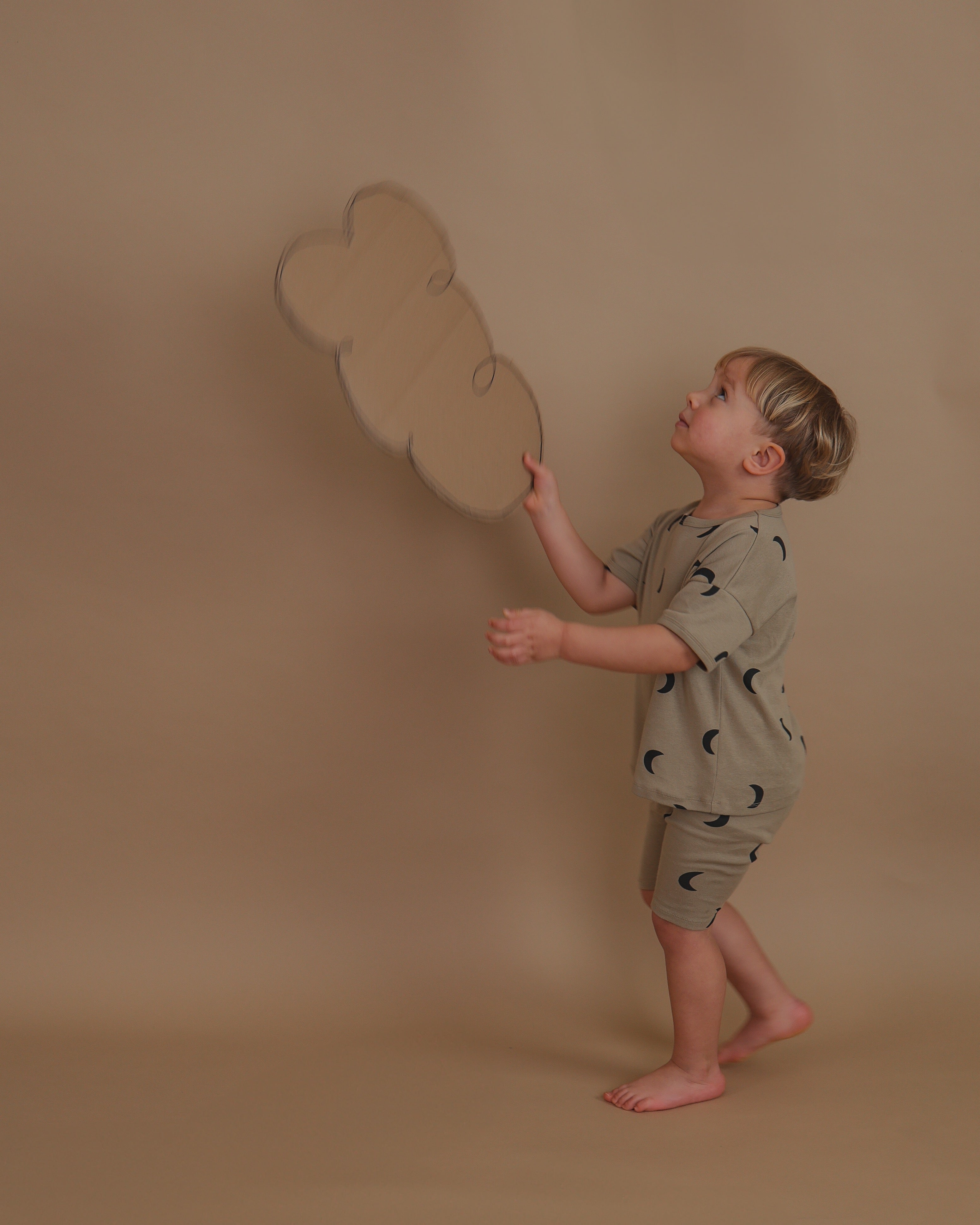 toddler in ribbed cotton boxy t-shirt in beige with moon print playing with cardboard cloud