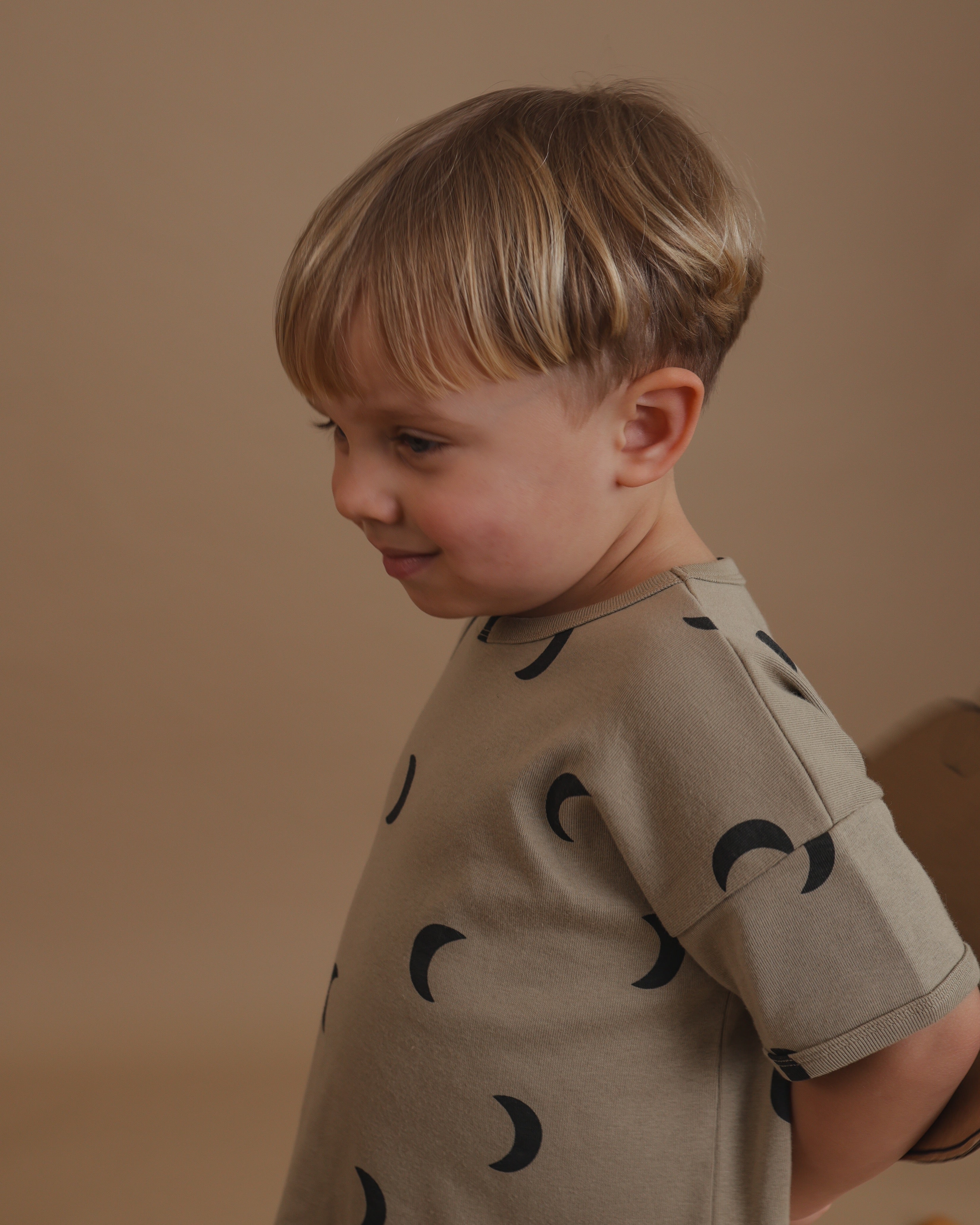 smiling toddler wearing dusky beige drop shoulder boxy t-shirt with black crescent print