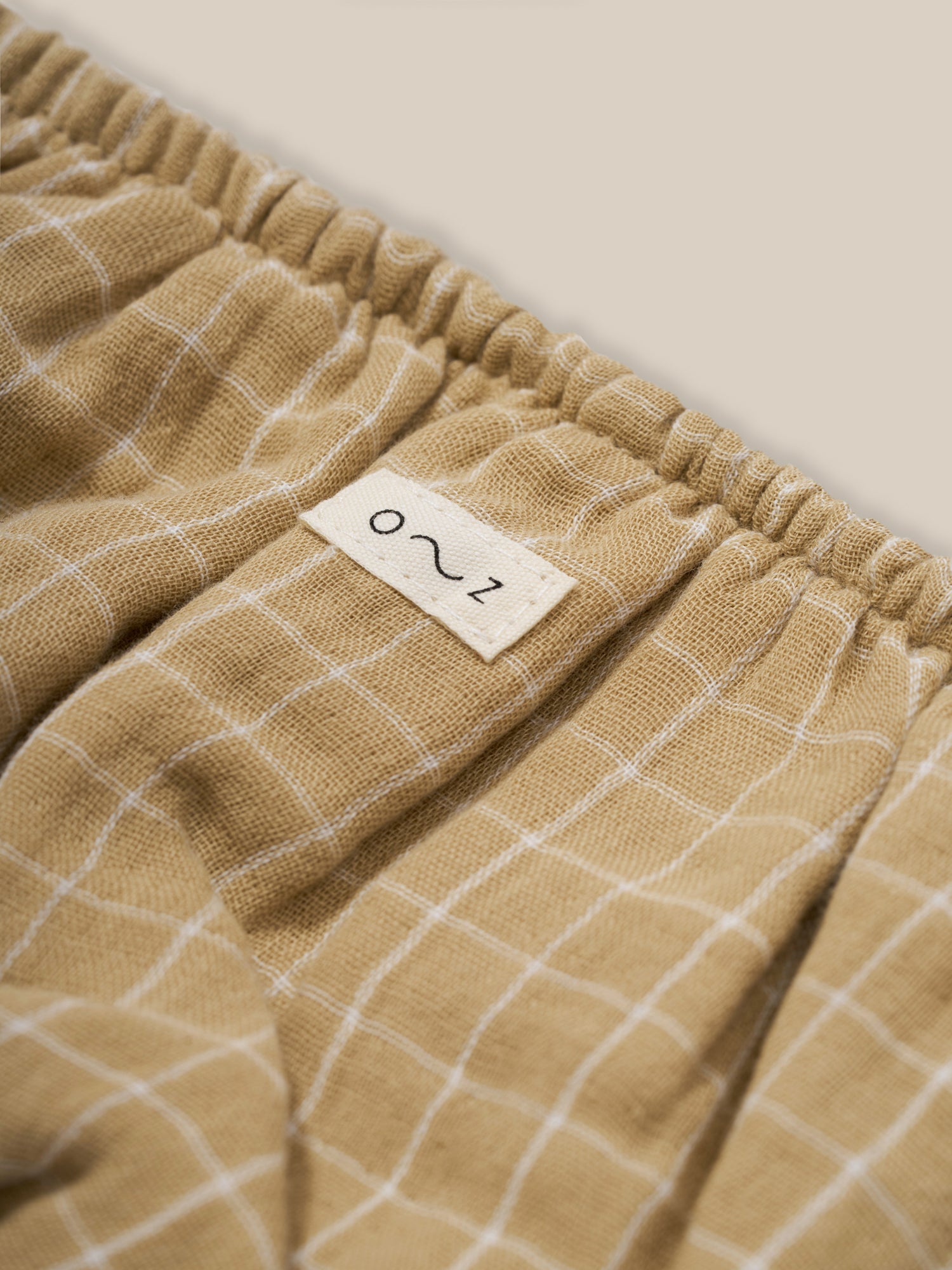 close up of baby & toddler organic muslin shortie in wheat gold grid check pattern