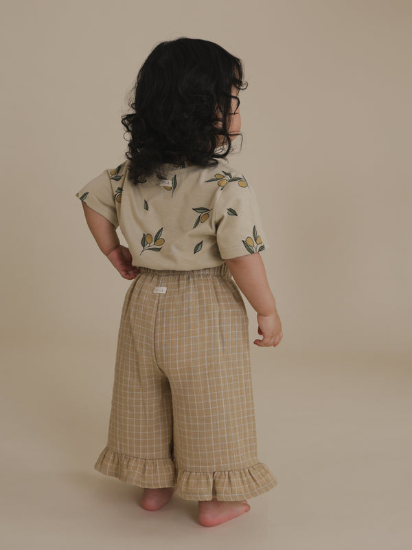 back view of toddler in soft muslin frill gold grid check culottes & t-shirt with one hand on waist