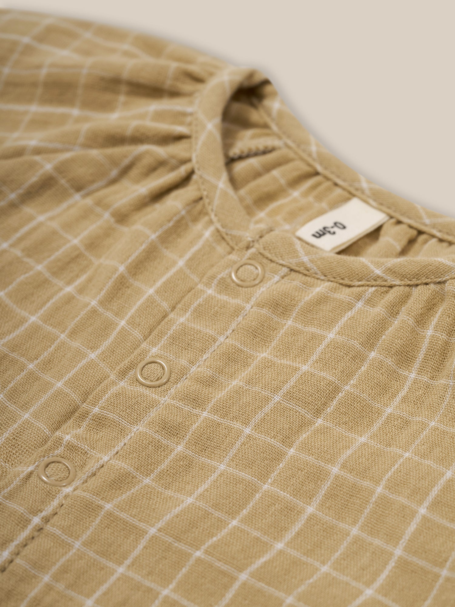 close up of baby wheat gold grid check organic muslin onesie gathered neckline & front poppers