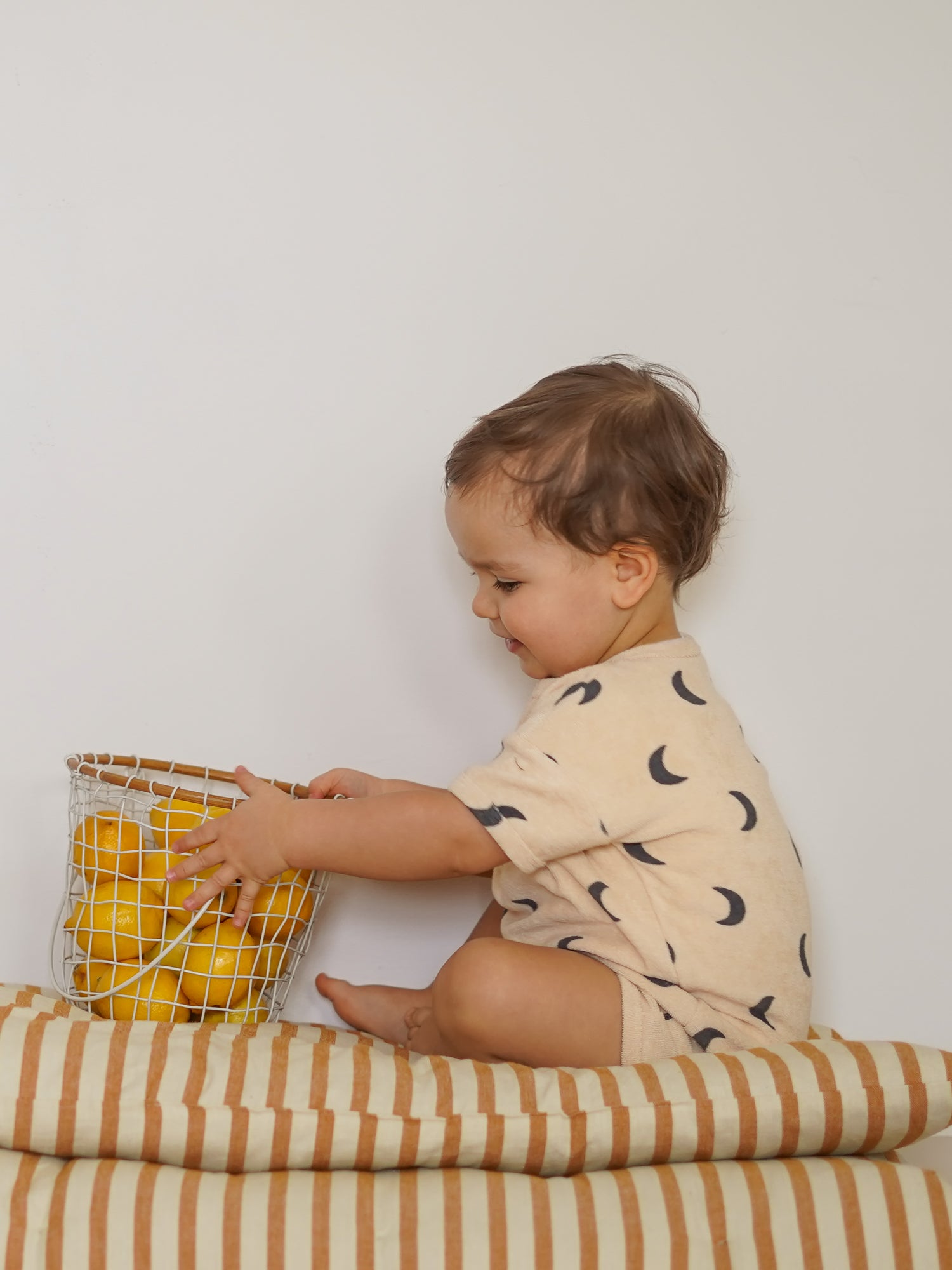 toddler wearing pebble midnight terry beach romper sitting on a striped mattress
