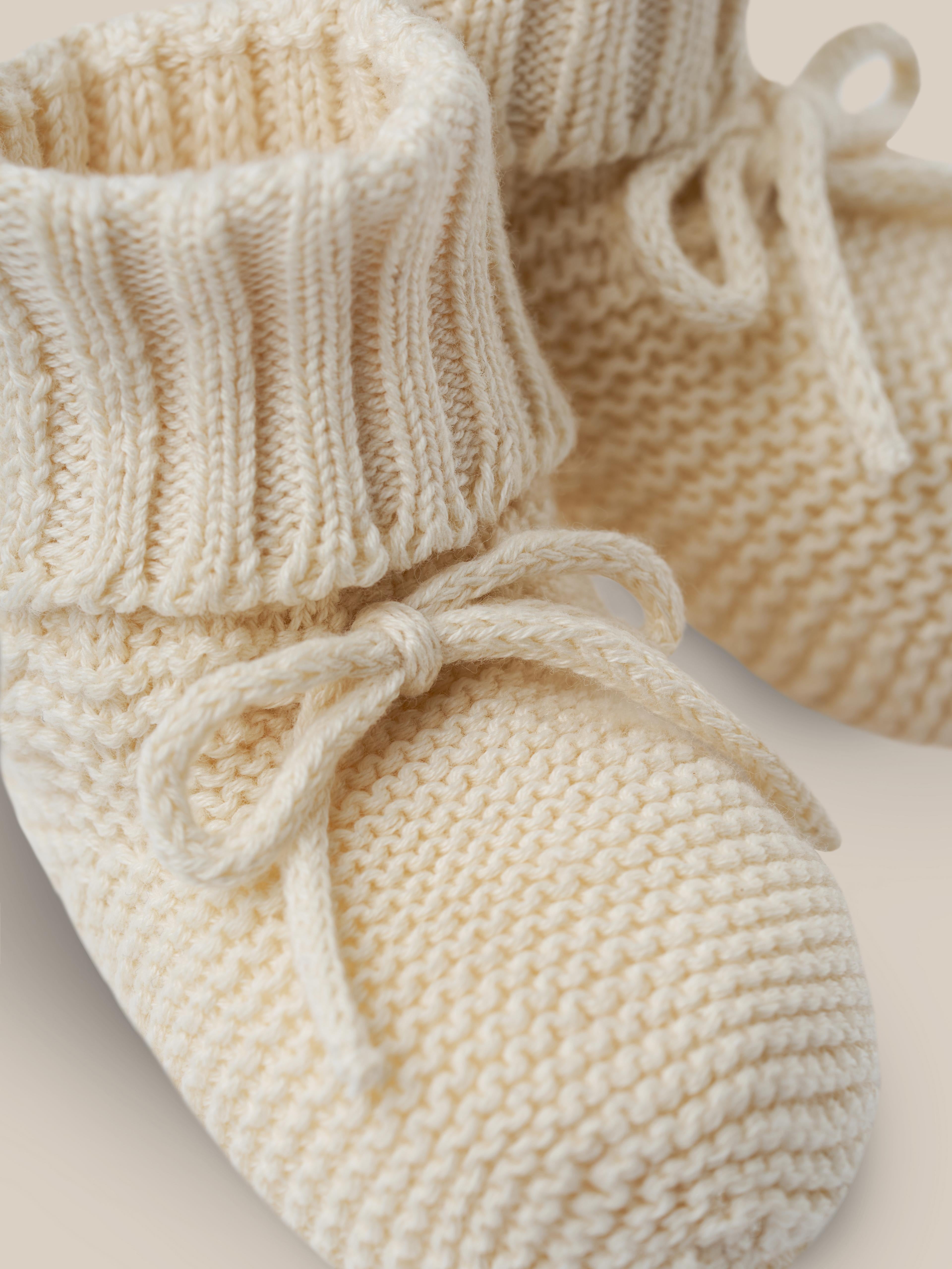 close up of undyed cotton knitted booties in cream with ribbons