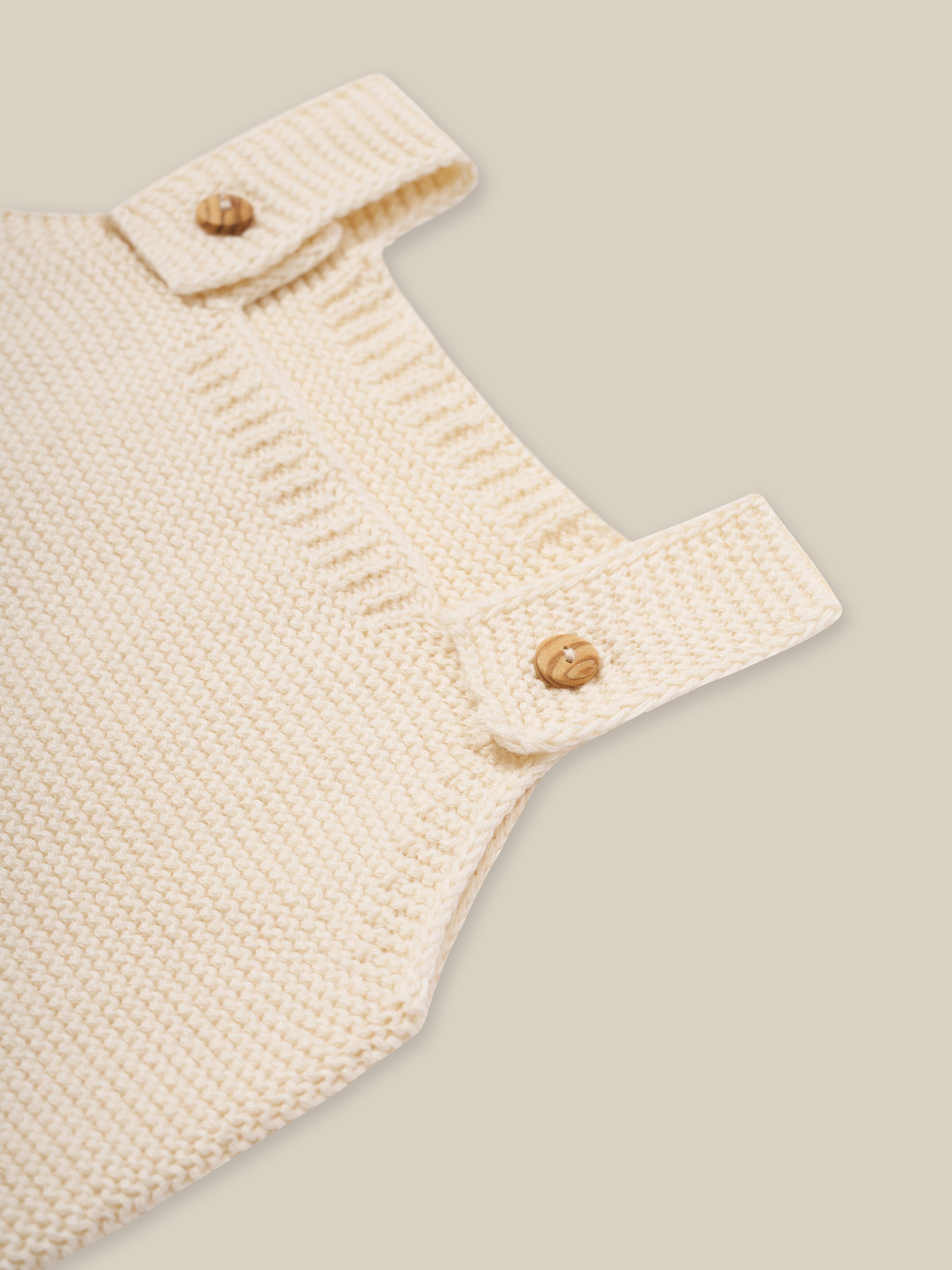 close up of undyed cotton knitted salopette in cream with wooden buttons