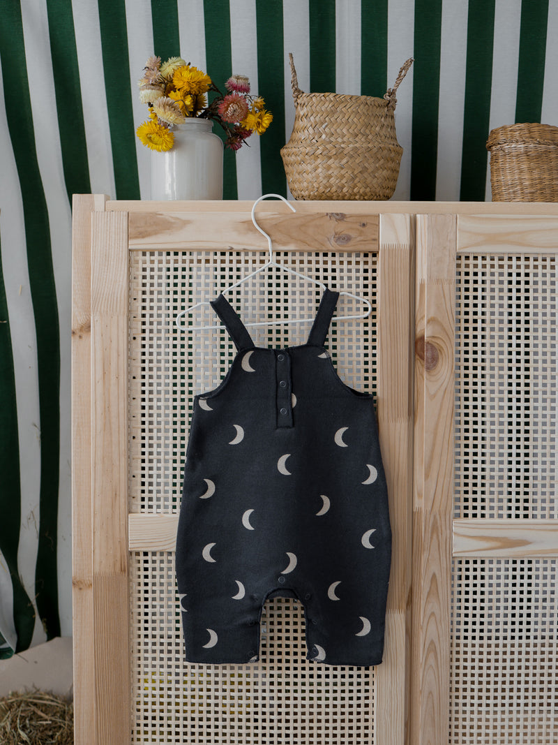 baby & toddler salopette in black with cream moons & poppers hanging on rattan wardrobe door