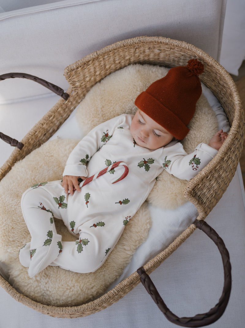 baby in christmas holly & candy cane footed sleepsuit in cream & beanie sleeping in moses basket